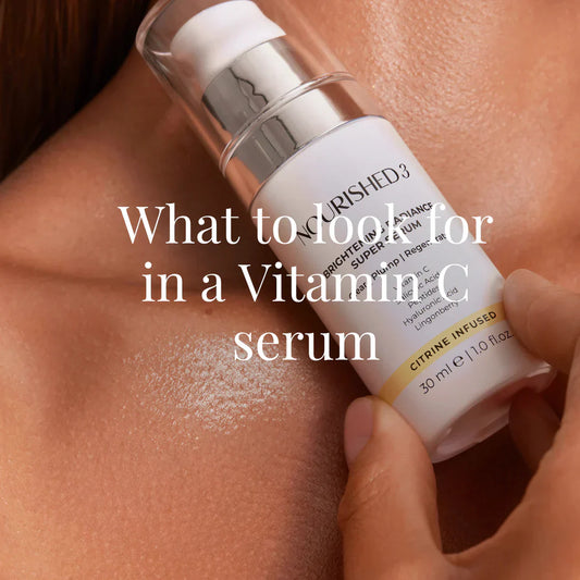 Close-up of a person’s hand holding a Nourished3 Vitamin C serum bottle near their dewy, glowing skin.